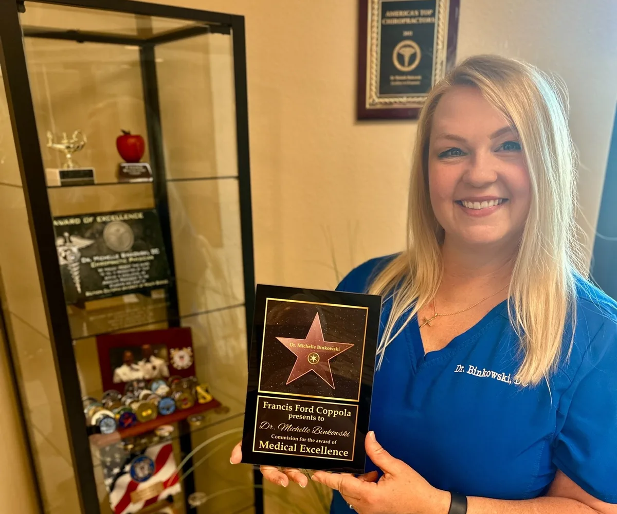 Dr. Michelle Binkowski beside a display case of military challenge coins and service memorabilia at Back in Action Chiropractic in Las Vegas